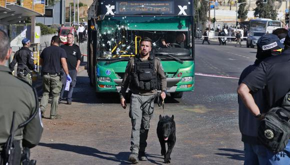 Un miembro de las fuerzas de seguridad israelíes sostiene un perro rastreador en la escena de una explosión en una parada de autobús en Jerusalén el 23 de noviembre de 2022. (Foto de Menahem KAHANA / AFP)