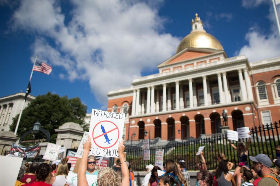Activistas contra las vacunas sostienen carteles frente a la Casa del Estado de Massachusetts durante una protesta contra el mandato del gobernador Charlie Baker. (AFP/Scott Eisen).