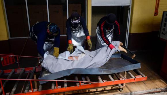 Empleados llevan el cadáver de una víctima de COVID-19 para poner en el horno crematorio. (EFE).