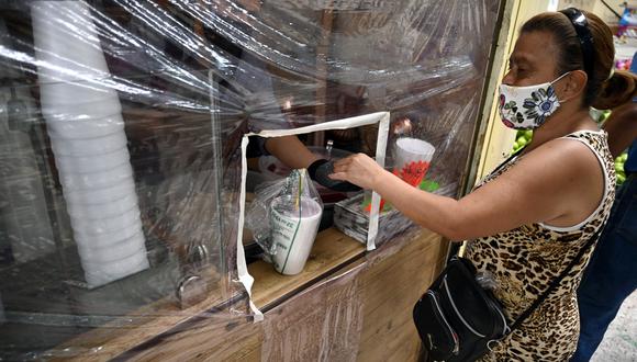Una mujer compra en una tienda a través de una protección plástica para evitar la propagación del nuevo coronavirus, COVID-19, en el Mercado Martínez de la Torre en la Ciudad de México. (Foto: AFP/ALFREDO ESTRELLA)