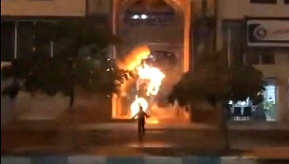Un manifestante colocando un objeto en la entrada del Seminario Khomeini en la ciudad iraní de Bushehr, antes de huir de la escena cuando el objeto estalla en llamas. (Foto de UGC / AFP)