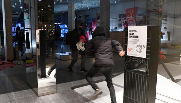 Los manifestantes se van tras romper el escaparate de una tienda y sujetar ropa durante los enfrentamientos tras una manifestación contra el encarcelamiento del rapero español Pablo Hásel, en Barcelona. (Pau BARRENA / AFP)