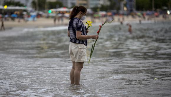 Una mujer reflexiona antes de arrojar flores a Iemanja, diosa del mar, en la playa de Copacabana en vísperas de Año Nuevo, en Río de Janeiro, Brasil, el 31 de diciembre de 2021. (Foto de Daniel RAMALHO / AFP)
