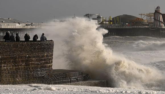 La gente reacciona cuando las olas rompen sobre un espigón en la playa de Brighton, en el sur de Inglaterra, el 18 de febrero de 2022, cuando la tormenta Eunice trae fuertes vientos en todo el país. (Foto de Glyn KIRK / AFP)