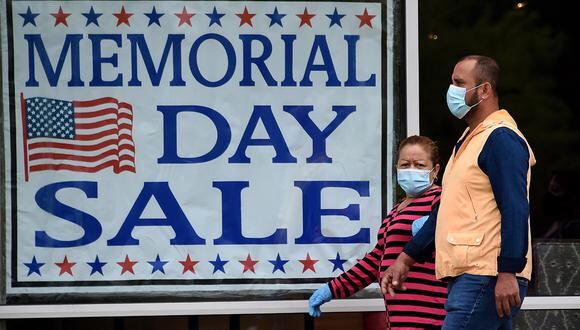 Las personas que llevan máscaras faciales pasan junto a un cartel que anuncia una venta de Memorial Day a medida que más empresas reabran en medio de la pandemia de coronavirus, en Arlington, Virginia. (Foto: AFP/Olivier DOULIERY)