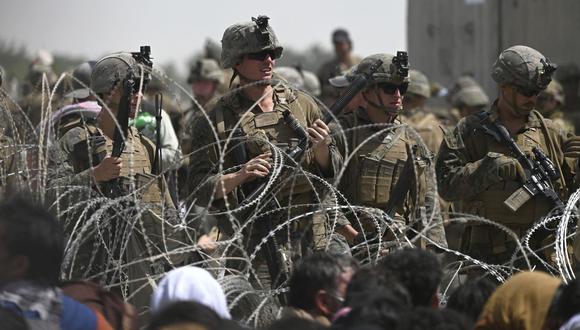 Los soldados estadounidenses montan guardia detrás de un alambre de púas mientras los afganos se sientan en una carretera cerca de la parte militar del aeropuerto en Kabul el 20 de agosto de 2021, (Wakil KOHSAR / AFP).