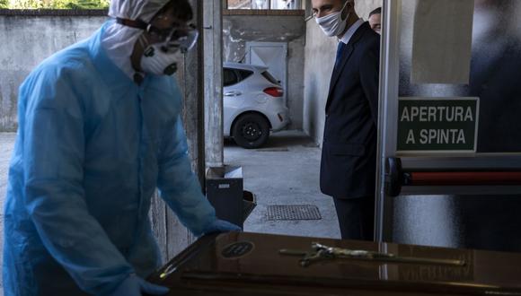 Un trabajador de la empresa funeraria "Palmero" mira a un colega que usa equipo de protección, llevando el ataúd de una víctima de COVID-19 en la morgue del hospital Saluzzo en Saluzzo, cerca de Cuneo, en el noroeste de Italia. (Foto: AFP/Marco Bertorello)
