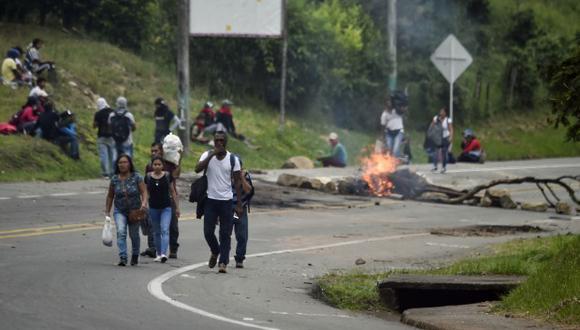 Un grupo de personas pasa por una barricada, establecida por indígenas para bloquear la carretera panamericana durante una protesta en La Agustina, área rural de Santander de Quilichao. (Foto: AFP)