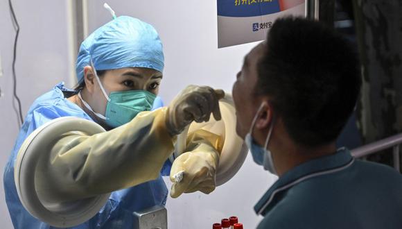Un trabajador de la salud toma una muestra de hisopo de un hombre para detectar el coronavirus Covid-19 en el distrito de Jing'an de Shanghái el 5 de julio de 2022. (Foto de Hector RETAMAL / AFP)