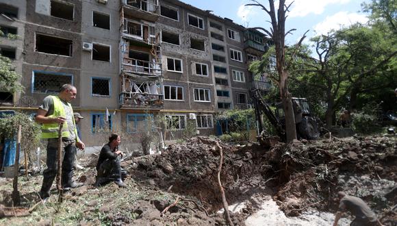 Los trabajadores de servicios comunales trabajan en un cráter después de un ataque con misiles frente a un edificio residencial en Kostyantynivka, óblast de Donetsk, el 15 de julio de 2022, en medio de la invasión militar de Rusia lanzada contra Ucrania. (Foto de Anatolii Stepanov / AFP)