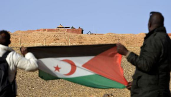 Hombres saharauis sosteniendo una bandera del Frente Polisario en el área de Al-Mahbes, cerca de los soldados marroquíes que custodian el muro que separa el Sahara Occidental controlado por Polisario. (Foto: AFP)