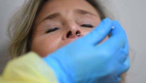Un asistente médico toma una muestra de hisopo para una prueba rápida de Covid en una mujer en un centro de pruebas y vacunación establecido en un concesionario de automóviles en Iserlohn, Alemania. (Foto: Ina FASSBENDER / AFP)