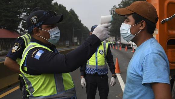 Imagen referencial. Un oficial de policía de tránsito verifica la temperatura de una persona como medida preventiva contra el nuevo coronavirus en Villa Nueva, Guatemala. (Johan Ordoñez / AFP).