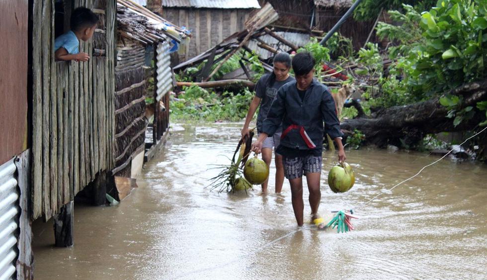 Filipinos caminan con cocos por una calle inundada en la localidad de Casiguran (Filipinas). (Foto: EFE)