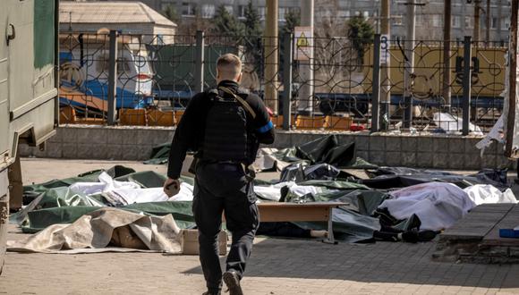 Un policía ucraniano camina hacia cuerpos cubiertos con láminas de plástico después de que un ataque con cohetes mató al menos a 35 personas el 8 de abril de 2022 en una estación de tren en Kramatorsk, al este de Ucrania, que estaba siendo utilizada para evacuaciones de civiles. (Foto de FADEL SENNA / AFP)