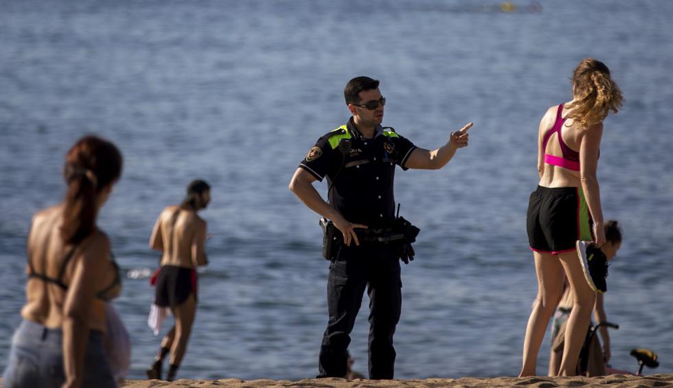 Un oficial de policía pide a las personas que no se sienten mientras patrullan en una playa de Barcelona, ​​España. (AP/Emilio Morenatti).