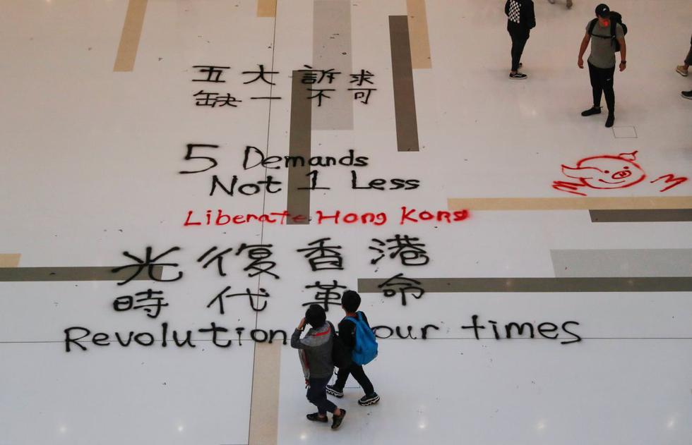 La gente pasa frente a los lemas de graffiti escritos en el piso de un centro comercial en Hong Kong. (Reuters)