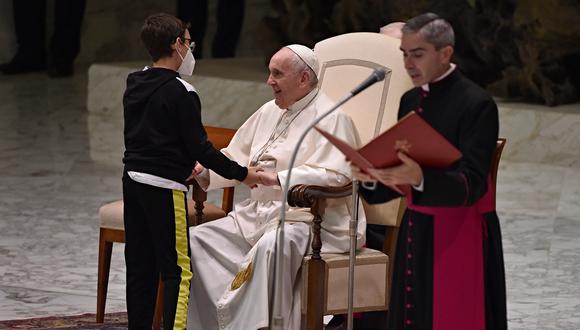 Francisco toma de las manos a un niño y lo sienta en una silla reservada a los cardenales. (Foto: ANDREAS SOLARO / AFP)