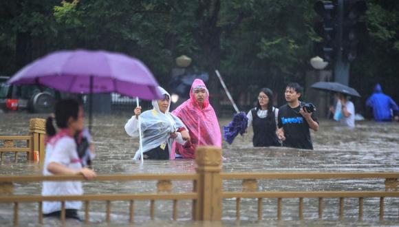 Esta foto tomada el 20 de julio de 2021 muestra a personas vadeando las aguas de una inundación a lo largo de una calle después de las fuertes lluvias en Zhengzhou, en la provincia central china de Henan. (Foto de STR / AFP).