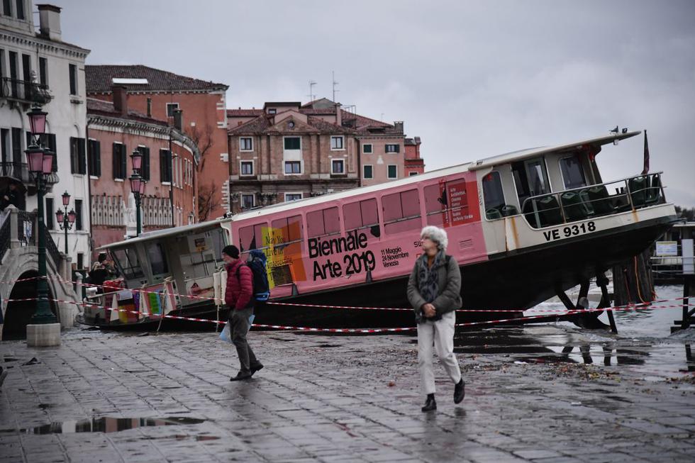 La gente camina junto a un bote de taxis varado en Riva degli Schiavoni, después de este fuera arrastrado durante la marea alta, "Alta Acqua", de la madrugada del 13 de noviembre. (AFP)