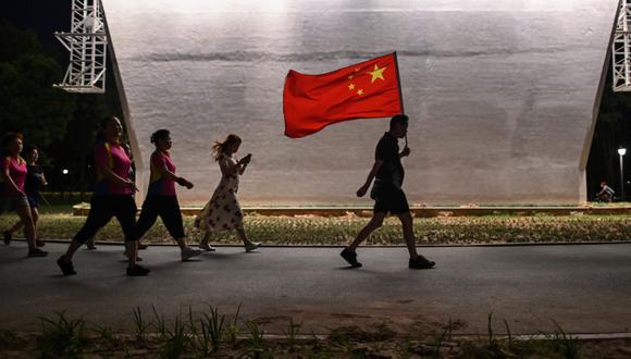 En esta foto tomada el 4 de septiembre de 2020, un hombre camina con la bandera nacional china en un parque junto al río Yangtze en Wuhan, provincia central china de Hubei. (AFP/Hector Retamal).
