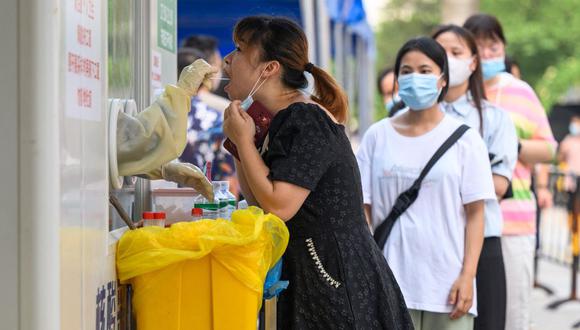 En esta foto de archivo tomada el 31 de julio de 2022, un trabajador de la salud toma una muestra de hisopo de una mujer para analizarla por el coronavirus Covid-19 en un sitio de recolección de hisopos en Guangzhou, en la provincia sureña china de Guangdong. (Foto por AFP)
