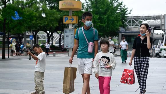 Un niño (izquierda) apunta con un rifle de juguete mientras una familia pasa caminando en Beijing el 12 de julio de 2022. (Foto de WANG Zhao / AFP)