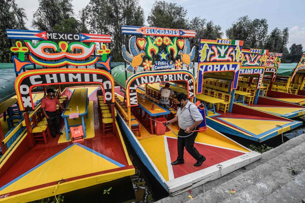 Un hombre desinfecta trajineras en el muelle del canal Cuemanco en Xochimilco, una red de canales y jardines flotantes que es uno de los principales atractivos turísticos de la Ciudad de México, durante su reapertura. (AFP/Pedro Pardo).