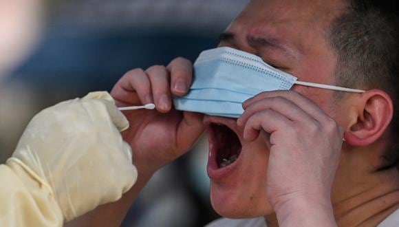 Un trabajador de la salud toma una muestra de hisopo de un hombre para detectar el coronavirus Covid-19 en el distrito de Jing'an de Shanghái el 13 de junio de 2022. (Foto de Hector RETAMAL / AFP)