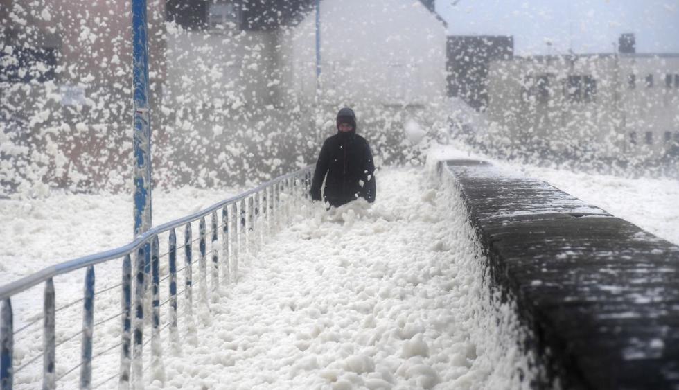 Una persona camina mientras la espuma del mar se lava en la pasarela en Saint-Guenole, oeste de Francia, mientras la tormenta Dennis se extiende por toda Bretaña. (AFP).