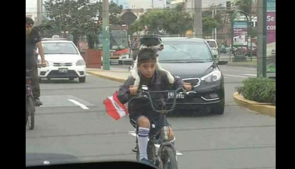 El niño y su mascota a bordo de una bicicleta y con una banderita peruana.