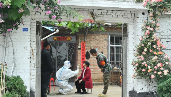 Esta foto tomada el 10 de mayo de 2022 muestra a un trabajador médico tomando una muestra de hisopo de un residente que no puede salir cómodamente para hacerse la prueba del coronavirus Covid-19 en su casa en Xiayi, en la provincia central china de Henan. (Foto de AFP)