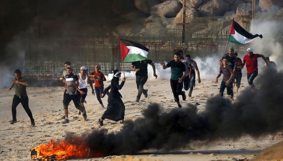Palestinos huyen del humo de gas lacrimógeno disparado por las fuerzas israelíes (fondo) en la playa cerca de la frontera marítima con Israel, en el norte de la Franja de Gaza. (Foto referencial: AFP)