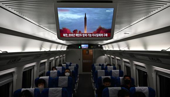 Los pasajeros se sientan en un tren debajo de un televisor que muestra una transmisión de noticias con imágenes de archivo de una prueba de misiles de Corea del Norte, en las afueras de Seúl el 2 de noviembre de 2022. (Foto de Anthony WALLACE / AFP)