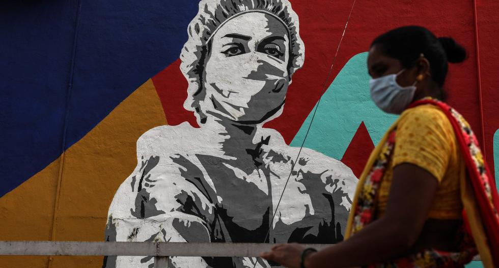 Una mujer con una máscara protectora camina frente a un graffiti en honor a los trabajadores de primera línea en la lucha contra la propagación del coronavirus, afuera de la estación de tren Mahim en Mumbai, India. (EFE/EPA/DIVYAKANT SOLANKI).
