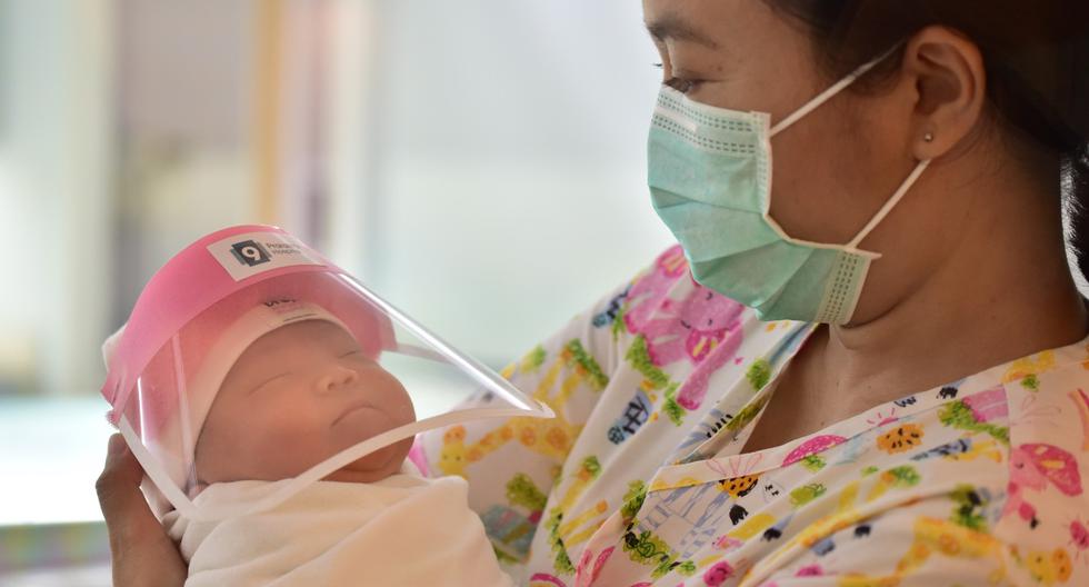 Imagen referencial muestra a una enfermera sosteniendo a un bebé recién nacido con un protector facial en un hospital de un país de Asia. (Lillian SUWANRUMPHA / AFP).
