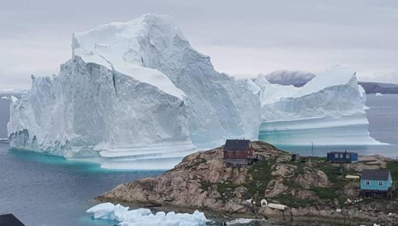 Un iceberg se aprecia detrás de edificios después de que se fundó en las afueras de la aldea de Innarsuit, un asentamiento isleño en el municipio de Avannaata, en el noroeste de Groenlandia. (Foto: AFP)