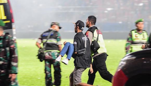 Esta fotografía tomada el 1 de octubre de 2022 muestra a personas corriendo con un espectador herido después de un partido de fútbol entre Arema FC y Persebaya en el estadio Kanjuruhan en Malang, Java Oriental. (Foto por AFP)