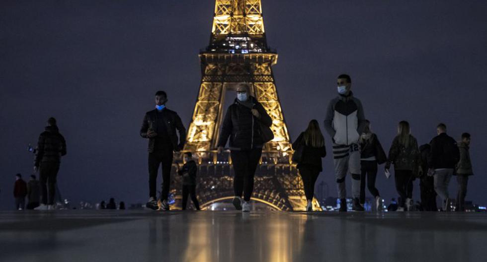 Personas con mascarillas protectoras caminan cerca de la Torre Eiffel al anochecer, pocas horas antes del toque de queda nocturno en toda la ciudad en París, Francia, 16 de octubre de 2020. (EFE/EPA/IAN LANGSDON).