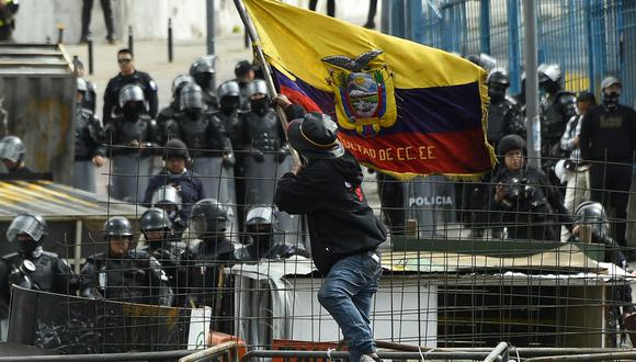 Un manifestante ondea una bandera nacional ecuatoriana mientras policías montan guardia en los alrededores de la Asamblea Nacional en Quito.