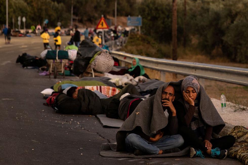 Una pareja se sienta cubierta con una manta mientras refugiados y migrantes acampan en una carretera después de un incendio en el campamento de Moria en la isla de Lesbos, Grecia. (REUTERS / Alkis Konstantinidis).