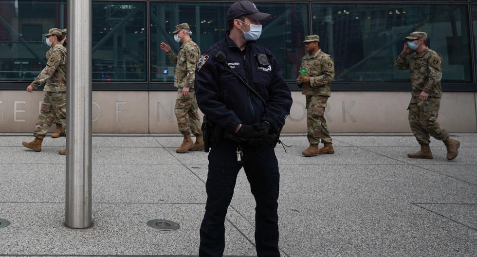 Los miembros de la Guardia Nacional del Ejército de EE.UU. caminan frente a un oficial de policía con una máscara afuera del Centro Jacob K. Javits en Nueva York. (Bryan R. Smith / AFP / Referencial).