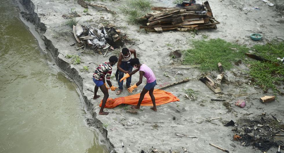 Los trabajadores de la corporación municipal mueven un cuerpo enterrado en una tumba poco profunda en las orillas del río Ganges durante la pandemia de coronavirus, el 25 de junio de 2021. (SANJAY KANOJIA / AFP).