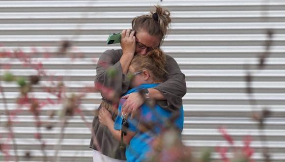 Una mujer llora y abraza a una niña mientras habla por teléfono afuera del Centro Cívico Willie de Leon, en Uvalde, Texas, el 24 de mayo de 2022, tras el tiroteo en una escuela primaria. (ALLISON DINNER / AFP).