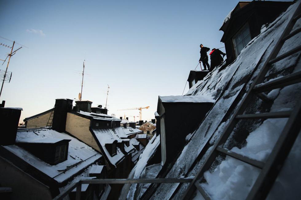 Encaramados a unos diez metros del suelo, Andrei (centro) y Alex quitan el espeso manto blanco que cubre el tejado de un edificio de Estocolmo, mientras su colega se asegura de que no caiga sobre los peatones. (Texto y foto: AFP).
