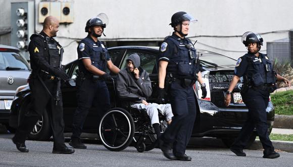 La policía escolta a un hombre en silla de ruedas del vecindario que rodea la escena de un tiroteo cerca de la cuadra 2900 de Van Ness Street en el noroeste de Washington, DC el 22 de abril de 2022. (Foto de Brendan SMIALOWSKI / AFP)