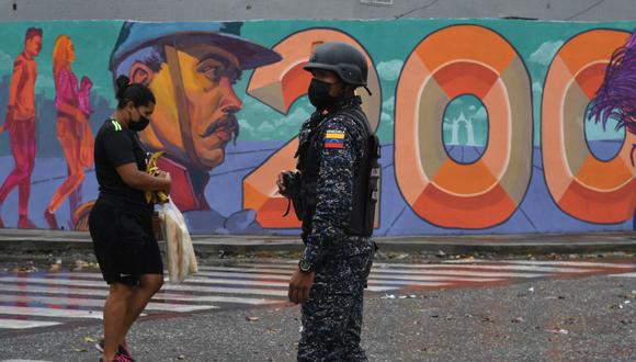 Imagen referencial. Un hombre que sostiene una bolsa con pan pasa por un miembro de la Policía Nacional Bolivariana durante enfrentamientos con presuntos integrantes de una banda criminal en los alrededores del barrio La Cota 905 de Caracas, el 9 de julio de 2021. (Yuri CORTEZ / AFP).