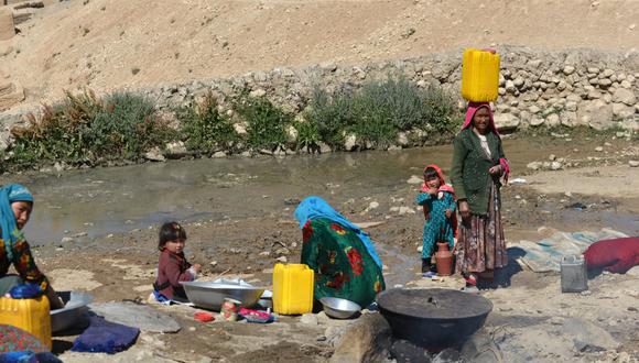 Mujeres afganas lavan ropa mientras los niños se sientan junto a un arroyo en la aldea Paytaw del distrito de Yakawlang de la provincia de Bamiyán el 15 de julio de 2022. (Foto de Ahmad SAHEL ARMAN / AFP)
