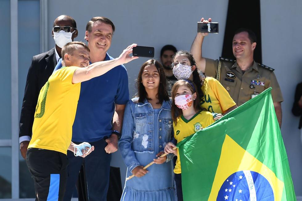 El presidente de Brasil, Jair Bolsonaro, y su hija Laura posan para una selfie con seguidores, frente al Palacio de Planalto en Brasilia, el 3 de mayo de 2020, durante la pandemia del coronavirus. (Foto: AFP/Evaristo Sa)