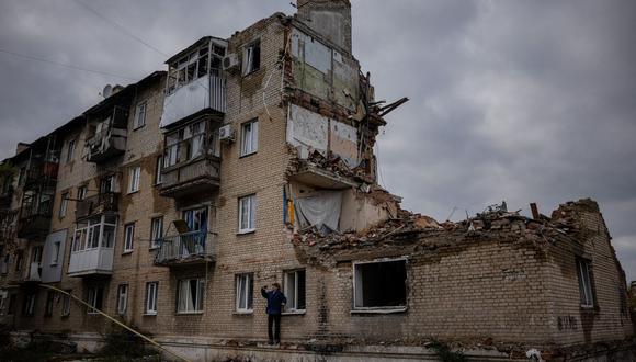 Un hombre toma fotografías con un teléfono junto a un edificio dañado en Lyman, región de Donetsk, el 21 de octubre de 2022, luego de que las fuerzas rusas recuperaran el área, en medio de la invasión rusa de Ucrania. (Foto de Dimitar DILKOFF / AFP)